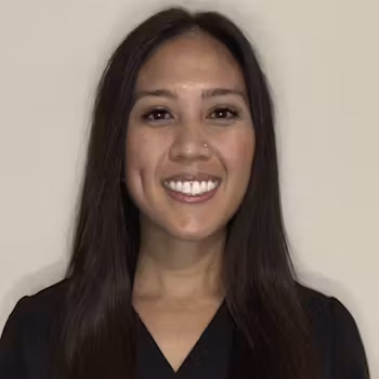 A woman with long, straight dark hair and a nose piercing smiles at the camera, wearing a black top against a plain light-colored background.